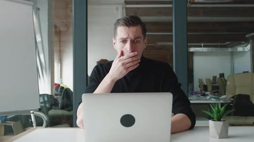 Gestresster Geschäftsmann ist schockiert, als er im Büro am Laptop arbeitet