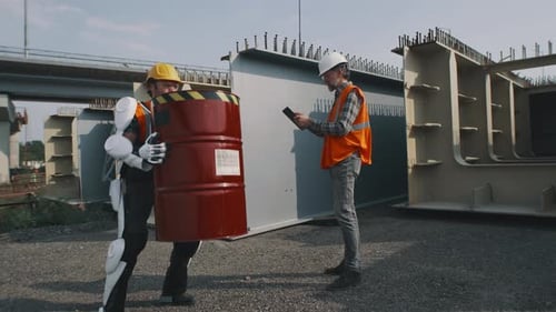 Worker Lifts Barrel Using Robotic Exoskeleton at Construction Site