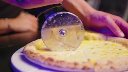 Pizza Cutter Slicing Four Cheese Pizza at Night