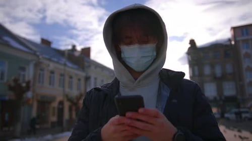 Hooded Young Adult Uses Phone in City Street