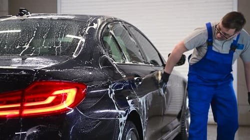 Car Detailing the Man Washes Backlights of a Car with a Hand Covered with a Special Wash Glove