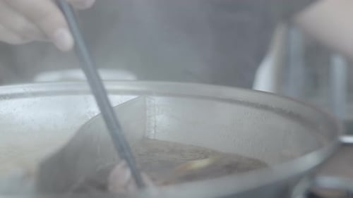 Una joven hembra que sostiene carne de res cortada con palillos come shabu a la hora del almuerzo.