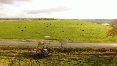 The tractor is stacking haystacks on an agricultural field in autumn, aerial view