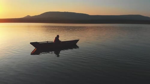 Lonely Man Sitting in a Boat on River on Sunset and Fishing