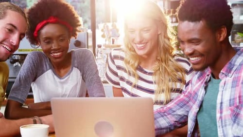 Friends Gathered Around Laptop in a Bright Cafe