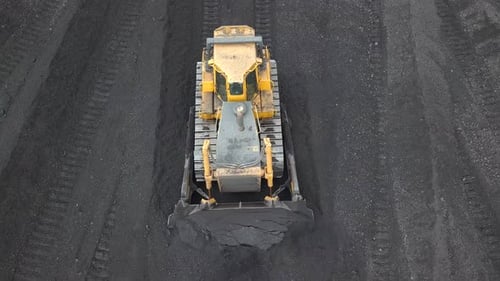 Bulldozer-Traktor sammelt schwarze Kohle auf Versorgungsfeld des thermoelektrischen Kraftwerks