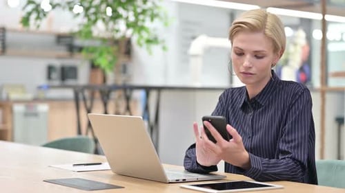 Businesswoman with Laptop Using Smartphone in Office