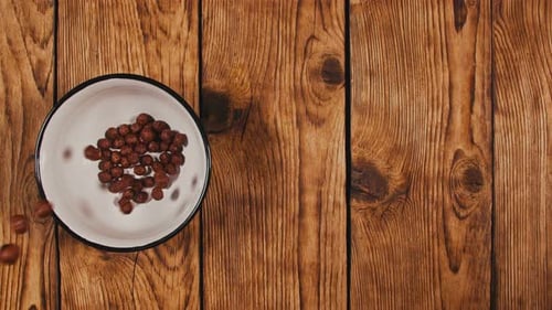 Brown Cereal Balls Falling into Bowl on Table