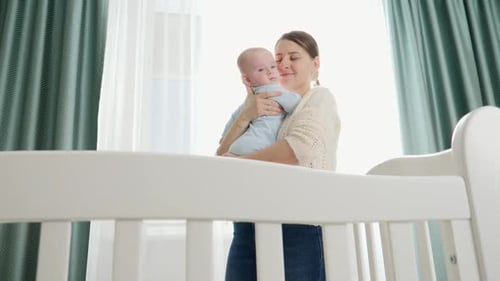Loving Mother Gently Holding Newborn Infant Near Crib
