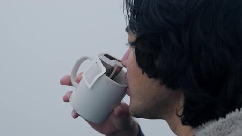 Young Man Drinks from Mug on Overcast Day