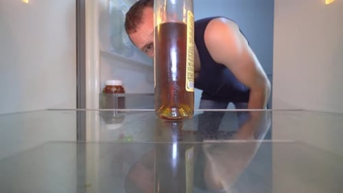 Man Opens an Empty Refrigerator and Examines Bottle