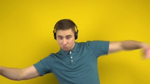 Young Man Dancing with Headphones on a Yellow Background. A Man in a Green Polo Is Listening To