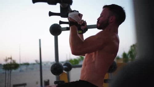Male shirtless athlete is working out at dusk, close-up of rising legs. Upper body exercise.