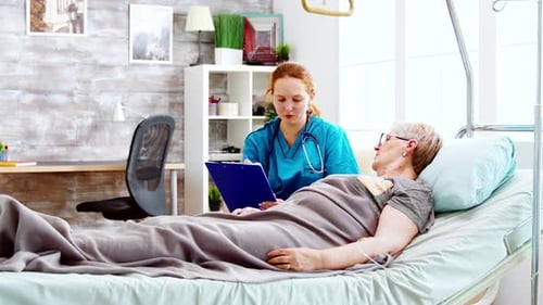 Social Worker Consulting an Elderly Disabled Woman Who Lies in Hospital Bed