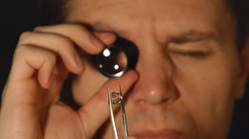 Expert Examining Jewel Through Magnifying Glass
