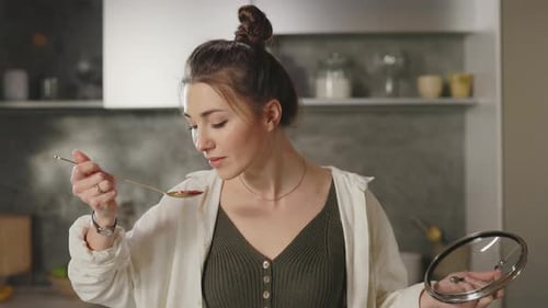 Woman Cooking and Tasting Food in Modern Kitchen