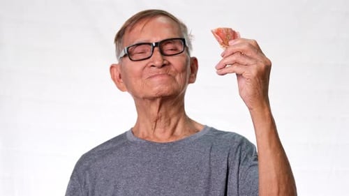 Le vieil homme asiatique sourit joyeusement montrant ses dents manquantes et tenant des prothèses dentaires à la main.
Santé