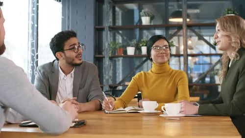 Cheerful Multiethnic Colleagues Speaking at Table in Restaurant