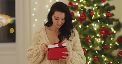 Woman Opening Christmas Present by the Tree