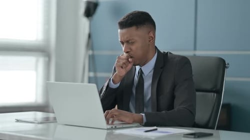 African Businessman Coughing while using Laptop in Office