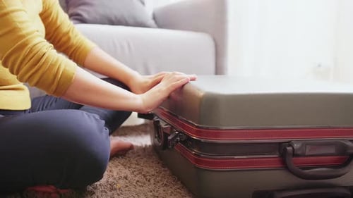 Woman Closes Suitcase on Floor, Preparing for Travel