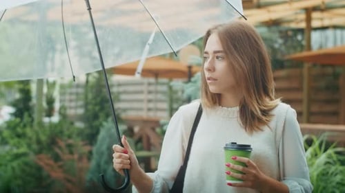 Joyful Girl Drinks Tea on the Street in Rainy Weather and Speaks on the Phone