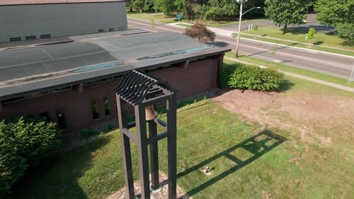 Luftaufnahme der Glocke außerhalb des Kirchengebäudes. Stabile Stahlpfosten werfen Schatten auf das Gras.