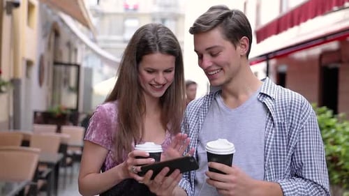 Smiling Couple Looking at Phone with Coffee