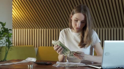 Mujer con calculadora contando dinero en dólares en casa