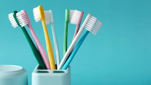 Colorful Toothbrushes in White Mug Against Light Green Background