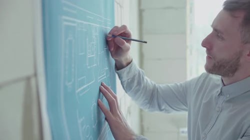 Young engineer-architect in a bright room works with blueprints near the wall