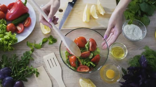 Mano femenina tomando un pedazo de tomate con una cuchara de madera y comiéndolo, ensalada fresca