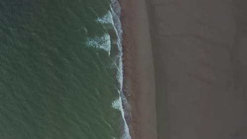 Slow Aerial Overhead Top Down Birds Eye View of Green Ocean Water and Brown Beach