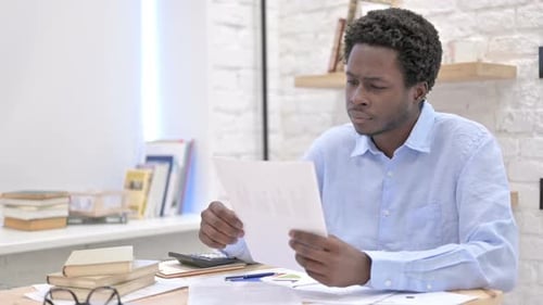 Worried Young Adult Reviewing Paperwork at Desk