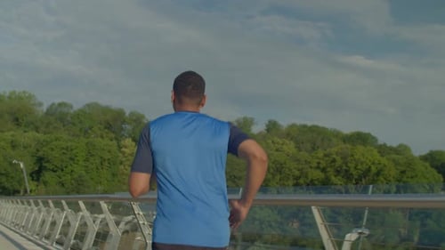 Rear View of Sporty Fitness African American Man Jogging on Bridge at Dawn