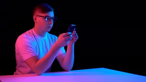 Young Man with a Smartphone. A Man Is Using a Telephone. Blue and Red Light Falls on a Man