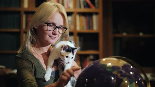 Woman Holding Cat Studies Globe In Home Library