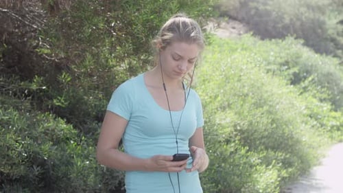 A young woman runner putting on earbuds before going on a run.