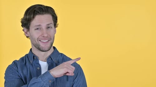 Man Pointing to Side Smiling on Yellow Background