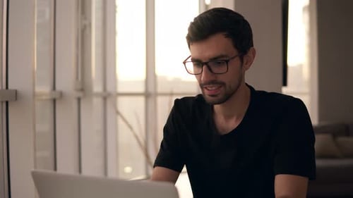 Young Adult Typing on Laptop by Window