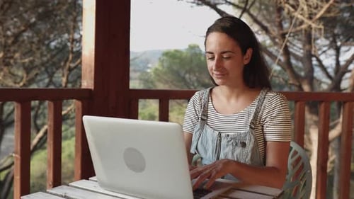 Junge Frau arbeitet am Laptop, während sie auf der heimischen Terrasse sitzt