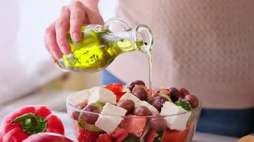 Greek Salad Preparation Series Concept Woman Pouring Olive Oil Into Bowl with Chopped Vegetables
