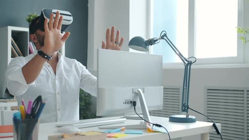 Slow Motion of Young Guy Wearing Virtual Reality Glasses Moving Arms in Office at Desk