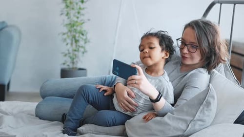 Woman and Child Relaxing with Smartphone on Bed