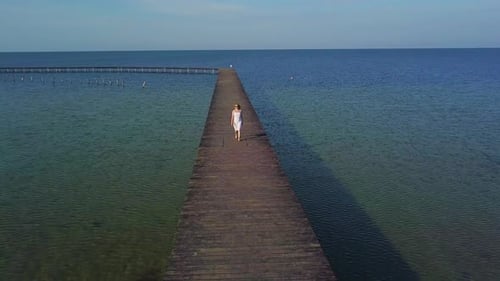 A Girl Walks on a Wooden Pier Near the Sea