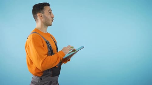 Construction Worker Looking Around, Taking Notes on Tablet. Isolated on Blue Background with