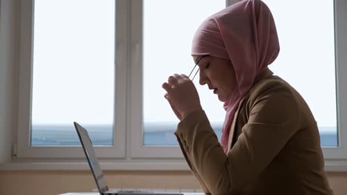 Woman in Pink Hijab Takes a Break and Massages the Bridge of Nose While Working on a Laptop