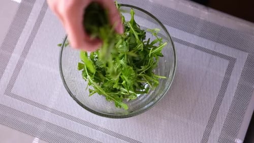 Mujer de estilo de vida saludable vertiendo rúcula en un tazón de vidrio