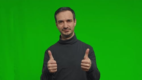 A Man Enthusiastically Shows a Thumb Up with Both Hands Over Isolated Green Background
