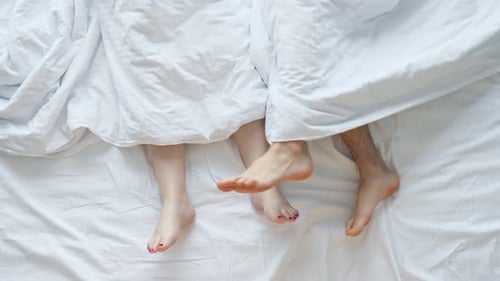 Couple Relaxing in Bed Under White Sheets